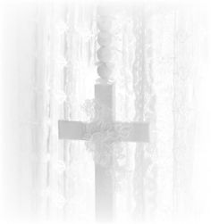 a cross on a window sill in front of curtains with white laces behind it