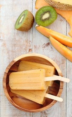 popsicles with kiwi and orange slices in a wooden bowl on a white table