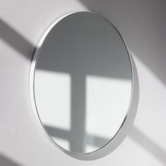 a white wall with a round mirror on it's side and the shadow of a cross on the wall