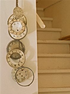 a clock hanging from the side of a wall next to a stair case with three clocks on it