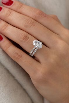 a woman's hand with red nail polish holding an engagement ring on her finger