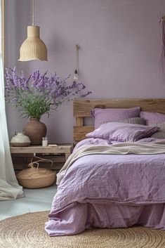 a bed with purple sheets and pillows next to a vase filled with lavender flowers on a table