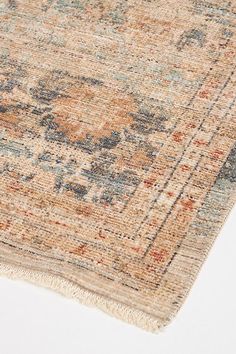 an old rug with faded colors and fringes on the bottom is laying on a white surface