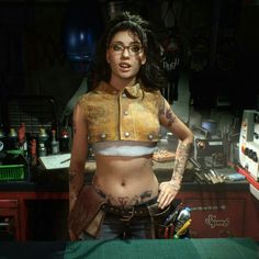 a woman with tattoos and piercings standing next to a table in a room filled with tools