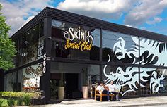 the front of a restaurant with people sitting on benches in front of it and trees