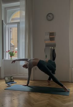 a woman doing yoga in front of a laptop computer on a wooden floor next to a window