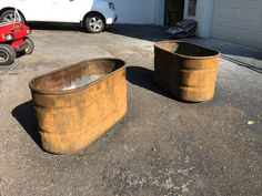 two rusty tubs sitting in the middle of a driveway next to a white car