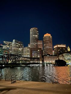 the city skyline is lit up at night with lights reflecting on the water and buildings in the background