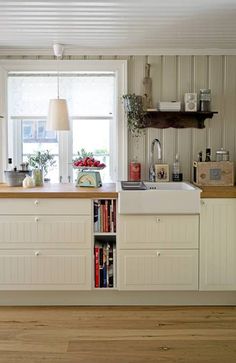 a kitchen with white cabinets and wooden flooring next to a window filled with flowers