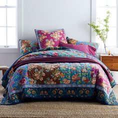 a bed covered in lots of colorful pillows and blankets