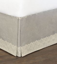 a white bed skirt with lace trim on the bottom and side edges, sitting on a hardwood floor