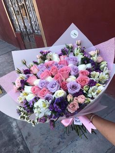 a bouquet of flowers is being held by someone's hand in front of a building