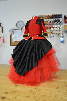 a woman in a red and black dress standing on top of a wooden floor next to a clock