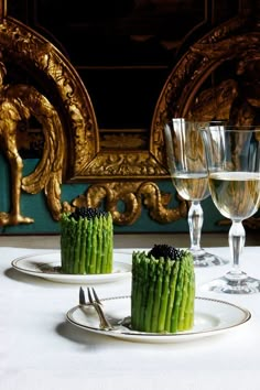 two desserts with asparagus and blackberries sit on white plates in front of an ornate gold frame