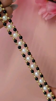 a close up of a person holding a necklace with pearls and black beads on it