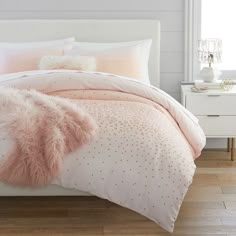 a white bed with pink and gold comforter set on top of wooden flooring