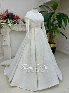 a white wedding gown on display in front of a table with flowers and potted plant