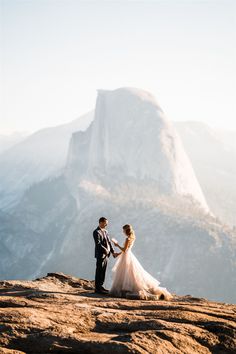 a bride and groom holding hands on top of a mountain in front of the mountains