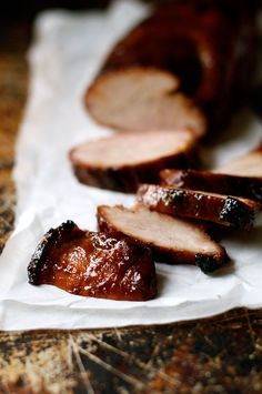 sliced meat sitting on top of a piece of wax paper next to other food items