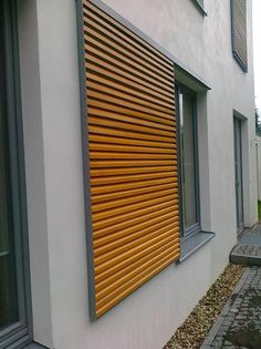 a white building with a wooden slatted window next to a brick walkway and sidewalk