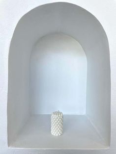 a white vase sitting in the middle of a room with an arch on it's side