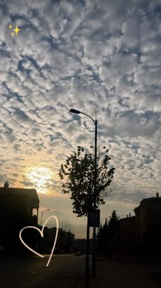 the sky is filled with clouds as the sun goes down in the distance, and there is a heart drawn on the street light pole