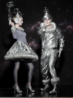 two people dressed in silver standing next to each other on a black and white background