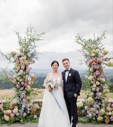 a bride and groom pose for a photo in front of an archway decorated with flowers