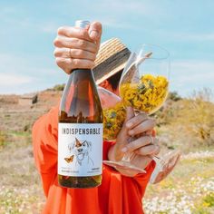 a person holding a wine glass with flowers in it and a bottle next to them