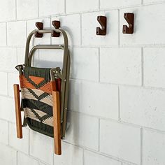 a wall hanging on the side of a white brick building with two hooks holding an old purse