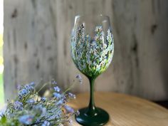 two wine glasses sitting on top of a wooden table next to blue and white flowers