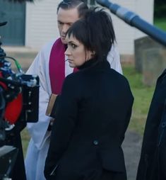 two people standing next to each other in front of a camera set up on the street