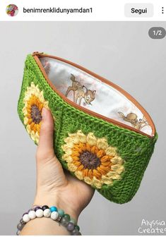 a hand holding a green crocheted purse with sunflowers on the inside