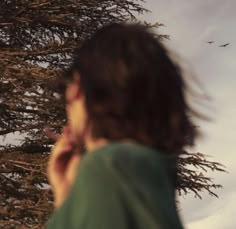 a man talking on a cell phone while standing in front of a tree with birds flying overhead