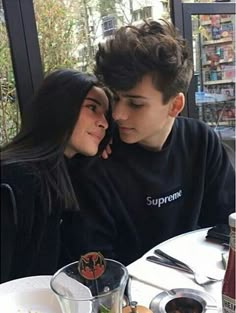 a young man and woman sitting at a table in front of a window looking into each other's eyes