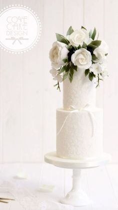 a white wedding cake with flowers on top is sitting on a pedestal in front of a white background