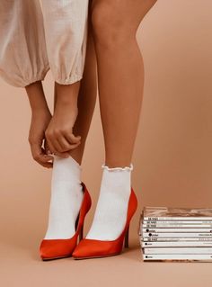 a woman's legs with red and white shoes next to stack of books