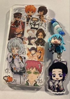 two keychains with anime characters on them sitting next to an iphone case that is shaped like the same character