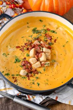 a bowl filled with soup and croutons on top of a table next to pumpkins