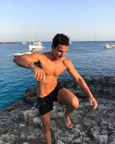 a shirtless man standing on rocks near the ocean