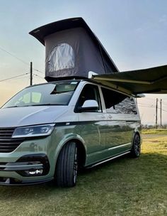 a green van parked in the grass with an awning on top