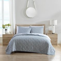 a bed with blue and white striped comforter next to a window in a room