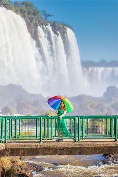 a woman with an umbrella standing on a bridge in front of a waterfall