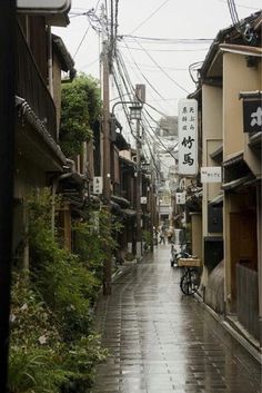 an alley way with buildings and power lines above it in the distance, on a rainy day