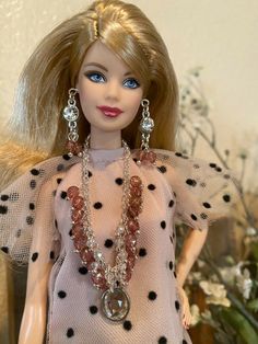 a barbie doll wearing a dress and necklace with pearls on it's neck, standing in front of a flower arrangement