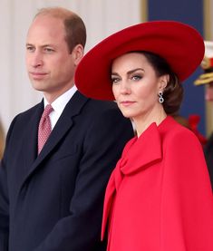 the royal couple are standing next to each other in red coats and hats at an event