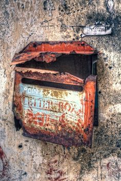 an old rusted out mailbox on the side of a building that has been vandalized