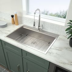 a stainless steel sink in a kitchen with marble counter tops and green cabinets next to a window