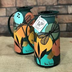 two green vases with dragonflies on them are sitting on a brown tablecloth