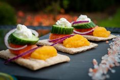 small crackers topped with cucumber, cream and other toppings sit on a table